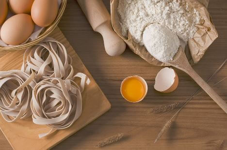 Flour, eggs, a rolling pin, and fresh pasta on a wooden table